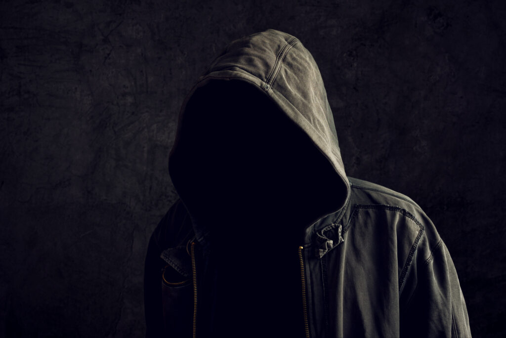 A faceless and unrecognisable man without identity wearing hood in dark room, spooky criminal.