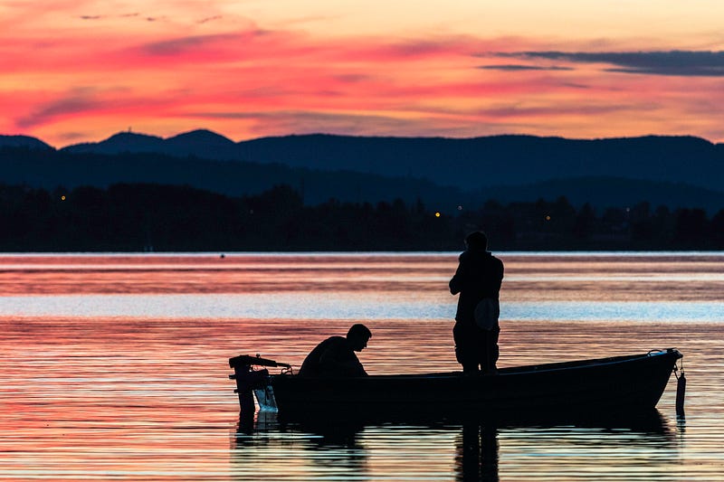 Two men fishing in a boat on a calm lake, with a brilliant orange sunset.