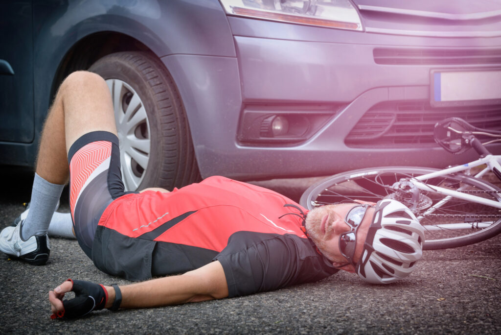 A cyclist lying on the road with injuries after being hit by a car.